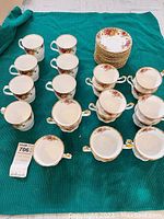 Overview of 7 straight-sided coffee cups and stack of saucers on green fabric