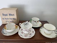 Four teacups and matching saucers displayed, showing different floral and decorative patterns including one Royal Albert boxed set