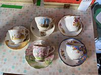 Top view of 5 teacups and saucers arranged on table, showing different floral and scenic designs