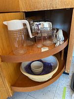Wooden corner shelf holding items including plastic pitcher, glass pitchers, toaster, measuring cups, bowls, electric cutter