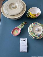 Overview of all items including covered floral bowl, four small white bowls with bee handles nested, pink flower spoon rest, and stacked yellow beehive measuring cups with colorful bee handles.