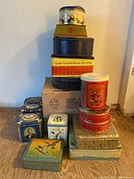 Full view of stacked and grouped vintage tins of assorted shapes and colors on the floor