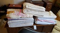 Stack of folded vintage blankets showing various white and pink striped patterns on top of a wooden chest.