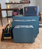 Full group photo showing three blue Travelgard suitcases of descending size with the cloth tote and leather briefcase on the side, plus a blue square case on top of largest suitcase.