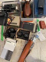 Overview of vintage cameras, View-Master viewers with original boxes, lens case, tripod in leather case, electronic calculator, and camera accessories on a table.