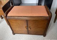 Front view of wooden bench with orange upholstered seat and double door cabinet with wooden knob handles.