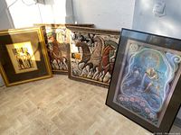 Four framed wall art pieces leaning against a wall on the floor, showing two quilted textile art and two framed prints.