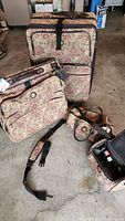Four pieces of floral pattern luggage including extra large rolling suitcase, folding suit bag, overnight bag and personal items bag on concrete floor.