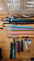 All 11 umbrellas arranged on floor showing variety of styles and colors including long-handle and folding types.