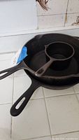 Three cast iron items stacked: two skillets and a melting pot on top, showing size and shape.