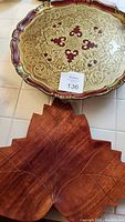 Photo showing large round red and gold painted wood tray with ornate gold embossing and scalloped edges, maple leaf carved wood tray underneath.