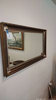 Front angle view of large rectangular mirror hanging on wall with ornately carved gold-tone frame.