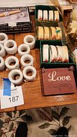 Photo of white marble napkin rings and boxed sets of ceramic napkin rings with poinsettia decoration, including a small hanging wooden 'Love' sign.