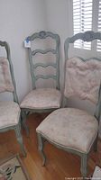 Four green painted mid-century ladder-back chairs with pink tie-on padded cushions arranged in a room corner.