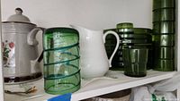 Photo showing stacked green glass cups and plates, white ceramic teapot and container with Wild Strawberry decals on shelf.