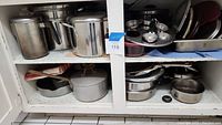 Image showing multiple large stainless steel pots and pans with lids filling two cabinet shelves.