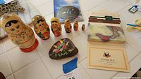 Full view of all items including 6 wooden Russian nesting dolls, painted rock, Italian recipe sheets and a spiritual CD.