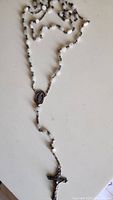 Full view of the rosary showing its white shell beads and silver links with the crucifix at the end.