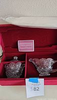 The set of leaded crystal creamer and sugar bowl with silver platter neatly placed in original red velvet box alongside the Crystal Legends by Godinger booklet.