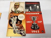 Four CFL magazines and programs from the 1960s laid flat on a table, covers showing players and Grey Cup images