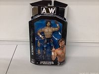 Front view of AEW Kenny Omega action figure in sealed packaging, showing figure and extra interchangeable hands.