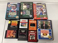 Photo of front view of Sega Genesis and Atari 2600 game cartridges with labels visible, arranged on a white surface.
