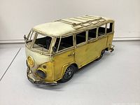 Front-side angle showing the metal Volkswagen bus model with yellow and off-white colors, roof rack and detailed front bumper.