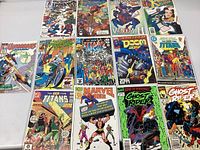 Overall overview of 15 various comic books laid out on a white table, all individually bagged and boarded. Titles include Spider-Man, Venom, New Teen Titans, Marvel Age, Ghost Rider, and Doom 2099.
