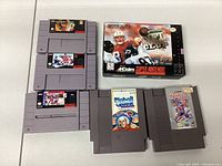 Four game cartridges including the NFL Quarterback Club 96 game cartridge (SNES) with original box in the background; also three additional SNES cartridges.