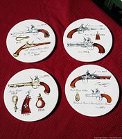 Four circular ceramic trivets displayed together on a red fabric background, each illustrated with historical English arms and accessories dated from the 1700s and 1800s.