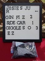 Front view of square letter board displaying sample text with black plastic letters. Bag of additional letters is visible below the board.