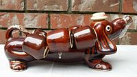 Side view of the brown ceramic dachshund decanter with attached cup sections along the body, showing glossy finish and ceramic detail.