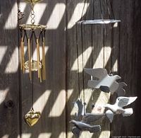 Both wind chimes hanging side by side against wooden background in natural sunlight