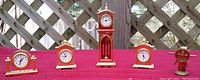Five miniature brass clocks and a ship wheel brass compass arranged on a red cloth with lattice background