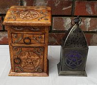 Wooden koa herb storage box featuring carved pentagrams, drawer with ring pull, and cupboard door. Metal pentagram lantern with colored glass beside it.