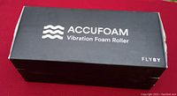 Black rectangular box labeled 'Accufoam Vibration Foam Roller FLYBY' placed on red surface