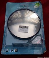 Photo of the large traffic safety mirror in original packaging including mounting bracket. The mirror is round with a black frame, convex surface and attached bracket.