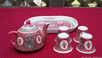 Full view of the mini Chinese red pottery teapot and four teacups arranged with the serving tray on a red cloth surface outdoors.