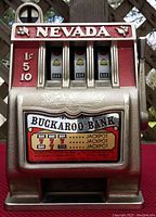 Front view of vintage metal slot machine with 'NEVADA' and 'BUCKAROO BANK' signage, showing reels with bar and bell icons, and pull arm.