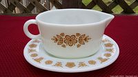 Gravy boat placed on saucer showing gold butterfly floral pattern on white glass