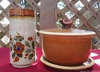 Photo showing both the covered casserole and the floral decorated vase side by side, with lattice background and red surface