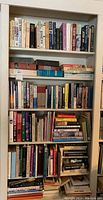 Full bookshelf filled with numerous hardback and paperback books packed on five shelves, arranged vertically and horizontally. Variety of book titles and genres visible.