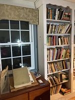 White bookshelf with six shelves filled with various books in different sizes and colors, showing overall lot contents from a right side angle.