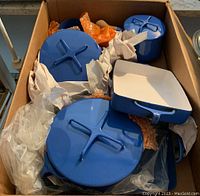 Top view of nested blue enameled cookware in box including three round lids and one square pan