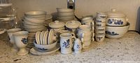 Wide view of the dinnerware set showing plates, bowls, cups, saucers, creamer, and canisters with lids all decorated with blue floral patterns.