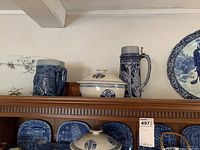 Top shelf items including a blue and white stoneware stein with metal lid, lidded canister, and several decorative plates.