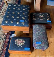 Set of four foot stools on wood floor showing their varied needlepoint and tapestry upholstered tops and wooden bases