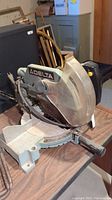 Full view of Delta compound miter saw on a table, showing base, blade guard, and handle.