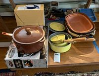 Overview of all cookware items showing brown cast iron pot with lid, yellow ceramic saucepans with lids and wooden handles, and terracotta roasting pans.