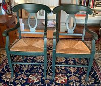 Pair of green painted wooden armchairs with rush seats on a patterned rug in a living room.
